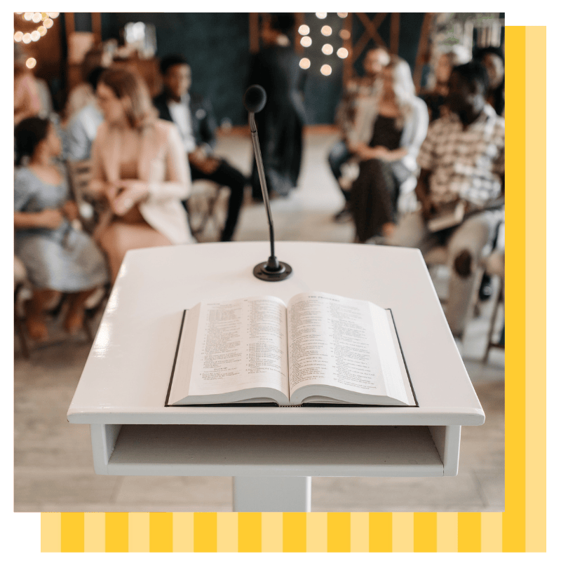 A Bible is open on a pulpit in front of a congregation of people at church