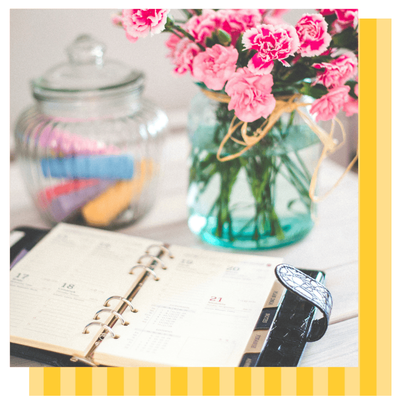 A planner lays open on a desk with flowers and office supplies